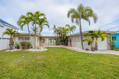 Coastal cottage with mature palms, breeze-block facade detail and manicured lawn.