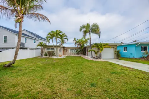 Street-level angle showing the expansive front yard, attached garage and palm-lined entrance.