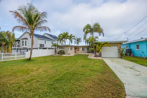 Angled view of the front yard and driveway flanked by mature palms and tropical foliage.