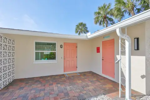 Coral-painted entry doors framed by breeze-block screens and palms.