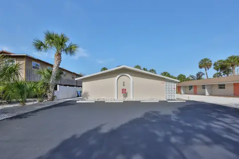 Side angle of the rear bungalow unit with fresh asphalt driveway and mature palm.