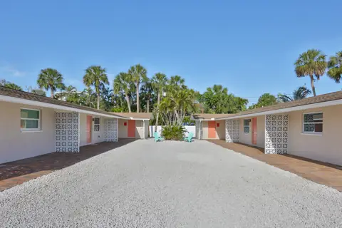 Shared gravel courtyard with tropical palms and coral-colored front doors.