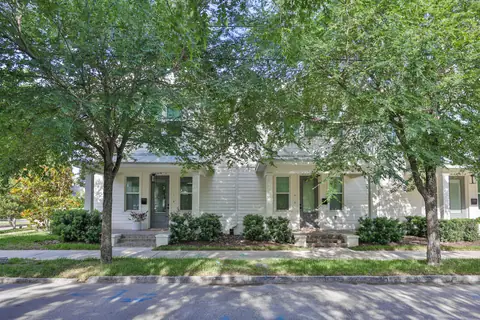 Front view of the white craftsman townhome with mature trees framing the facade.