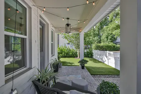 Charming covered porch strung with Edison lights overlooking a private artificial-turf yard.
