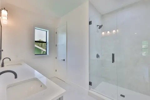 Primary bath with double quartz vanity, matte-black fixtures and frameless glass shower.