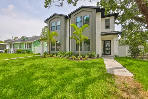 Modern farmhouse facade in sage green stucco and white siding with dramatic black-framed windows.