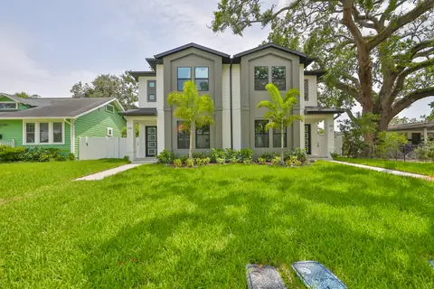 Secondary front view of the sage-and-white farmhouse framed by a live oak.