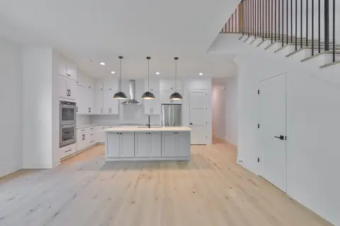 Two-story open kitchen with quartz island, industrial pendants, wall ovens and statement hood.