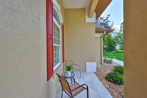 Covered front entry with red shutters, patterned tile paving and intimate seating nook.