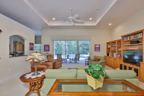 Open great room with tray ceiling, built-in bookshelves and sliding glass doors to the pool.