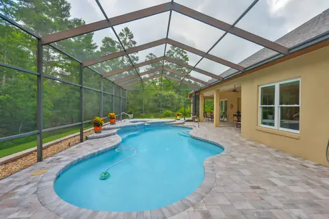 Screen-enclosed saltwater pool and spa with travertine decking, backing to private woods.