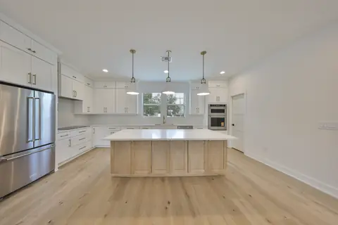 Open chef's kitchen with white cabinetry, oversized island and stainless wall ovens.