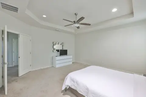 Primary bedroom with tray ceiling, plush carpet and soft natural light.
