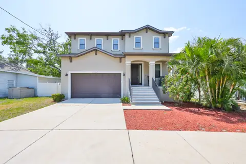 Front elevation with paver driveway, tropical landscaping and inviting covered entry.