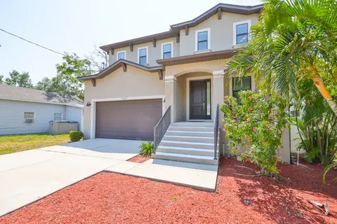 Close-in exterior view showcasing the home's stucco facade and mature tropical plantings.