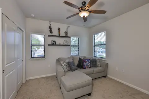 Cozy flex room with sectional seating, large windows and a modern ceiling fan.
