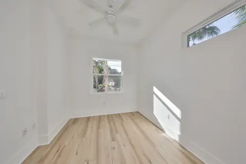 Compact bedroom with dual windows framing palm and sky views.